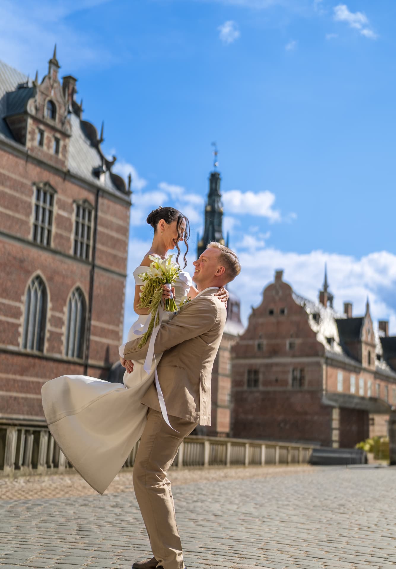 Groom lifting the laughing bride on the castle courtyard, joyful Frederiksborg Slot wedding photography Denmark